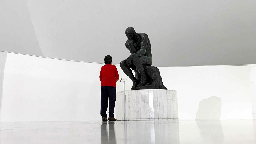 A young man looking at The Thinker statue by Auguste Rodin in a museum and wondering, what is man?