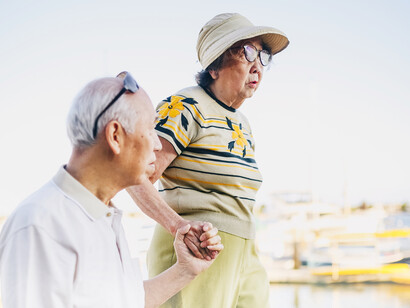 The husband holds his wife's hand as they walk along the river