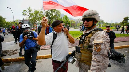 Un pacífico manifestante ondea una bandera chilena delante de un militar