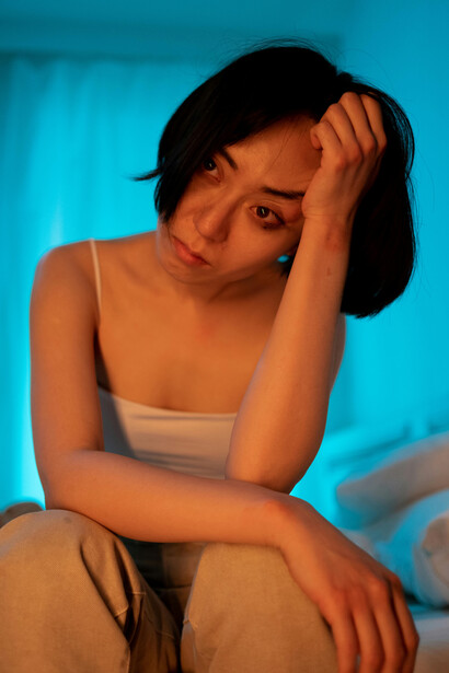 A short-haired woman in a white tank top appears upset, with her hand on her face