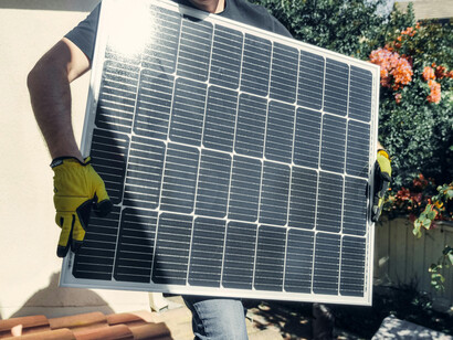 A man wearing a black shirt stands on a rooftop while holding a solar panel