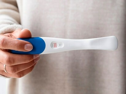 A woman’s hand holds a positive pregnancy test result, capturing the moment of joy