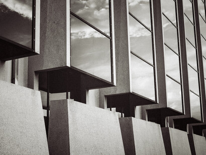 Vista arquitectónica en blanco y negro que enfatiza la repetición de ventanales salientes de cristal donde se reflejan las nubes del cielo