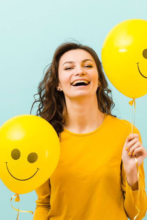 A joyful woman posing with a front view, holding balloons featuring smiling faces, embodying happiness