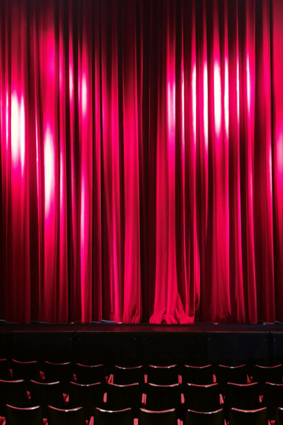 Red theatre chairs lined up beside rich red curtains in the salon