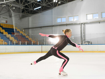 A girl in a pink and black long-sleeve bodysuit performs on the ice, illuminated by a spotlight in a cold, empty rink