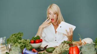 Woman holding a tablet and making a surprised face while looking at a table full of vegetables