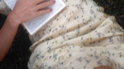 Teenage girl lying on the grass in a yellow sundress with a novel on her chest
