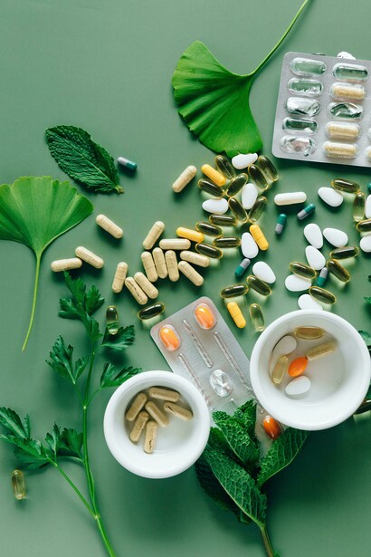 On a green table, capsules and leafy herbs reflect the growing interest in combining alternative medicine with daily multivitamins