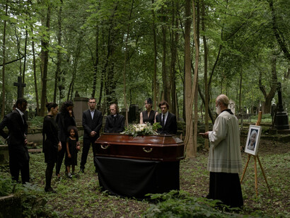A solemn forest funeral with mourners in black standing beside a brown coffin