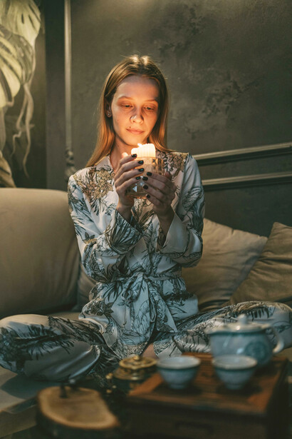 A woman meditates on a couch in a peaceful room, surrounded by soft indoor lighting