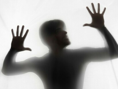 In the studio light, a figure fades into fragments, hands suspended between presence and disappearance