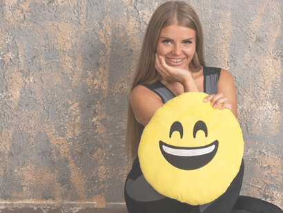 A young girl in sporty attire, clutching a smiling emoji pillow