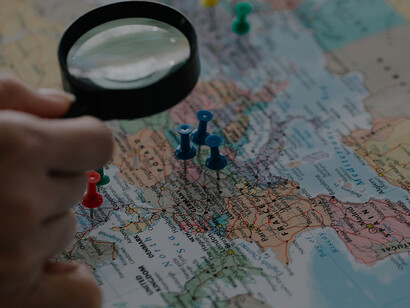Person looking at marked countries on map with magnifying glass