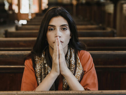 Woman in an orange long-sleeve shirt holding a black Bible while praying in church