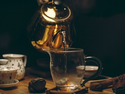 Hot water flows from a golden kettle into a teacup, beginning the tea-brewing process
