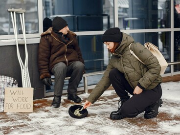 A woman donating money to a homeless individual during winter, symbolizing the vulnerability created by poverty and food insecurity