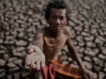 During the dry season marked by water scarcity and drought, an elderly man is captured in a poignant moment, earnestly beseeching for rainfall to alleviate the parched land