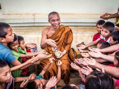 Buddhist monk distributing item to children 
