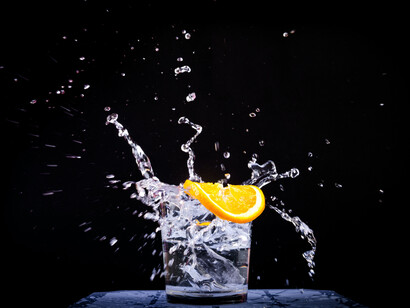 A short glass of water splashing with a slice of orange