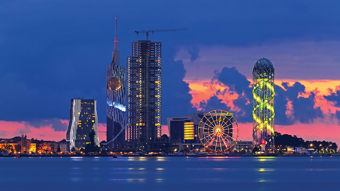 As the sun sets over Batumi, Georgia, the cityscape transforms into a mesmerizing tapestry of warm hues, casting a spellbinding glow over the charming coastal city