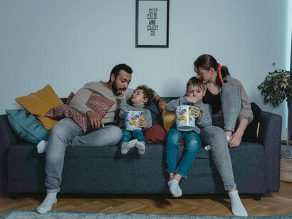 A man and a woman sit together on a blue sofa, sharing popcorn