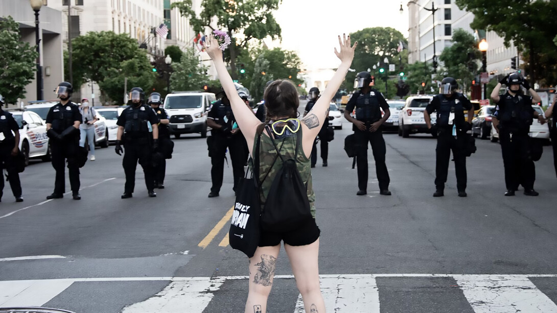 A woman in a green and black tank top raises her hands in protest