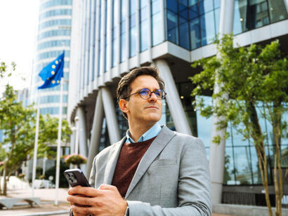 A smiling businessman uses a digital tablet for work outside a modern EU office building