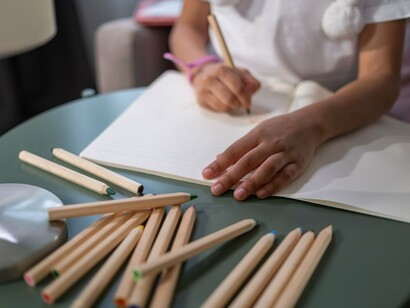 Uma criança desenha em um caderno branco, vista de perto enquanto transforma pensamentos em linhas e formas. No artigo, o papel aceita o que a criança consegue nomear, mas também revela aquilo para o qual não existe referência: um lugar paterno que permanece vazio