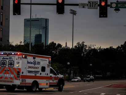 White and red ambulance truck with blaring sirens on the road during the daytime