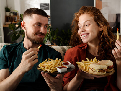 Happy woman looking at her boyfriend’s plate filled with fast food, illustrating the appeal of ultra-processed and junk foods
