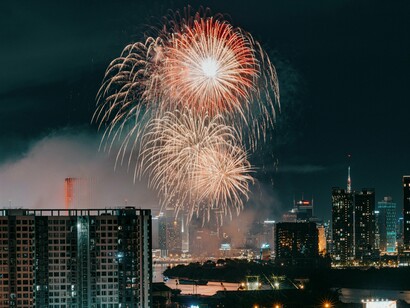 A burst of vibrant fireworks illuminates the night sky above Ho Chi Minh City, casting a celebratory glow over the urban skyline and the winding Saigon River, reflecting the city's dynamic spirit and festive atmosphere