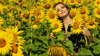 A woman in a black and white floral shirt stands in a sunflower field under the bright daylight, radiating inner peace and a positive mindset