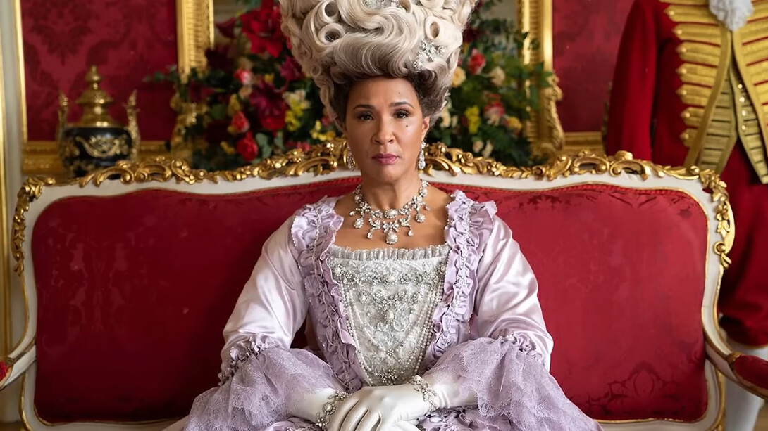 Queen Charlotte from Bridgerton seated in an ornate palace setting, representing the grandeur and unapologetic extravagance of Regency-inspired fashion