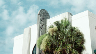 An art deco front face of a Miami building, and their notable palm trees