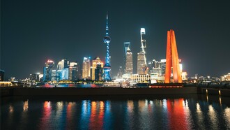 As luzes de Xangai iluminam o horizonte e se refletem nas águas da cidade durante a noite. A moderna paisagem urbana simboliza a retomada do protagonismo econômico chinês discutida ao longo do texto.