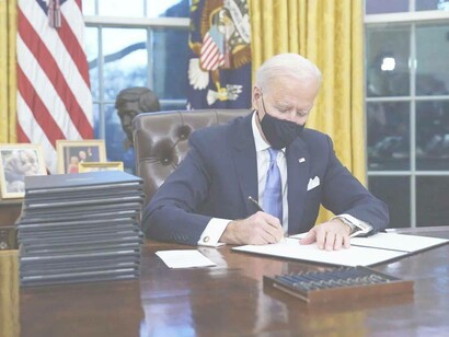 President Joe Biden signing his name to a letter that he has composed in the name of the country