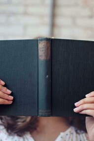 Mulher com livro aberto em frente ao rosto. Primeiro de tudo, vamos deixar claro: sim, qualquer leitura ajuda! E não, isso não é uma desculpa para se entupir de revistas de fofoca e achar que está tudo bem (apesar de que, se isso te faz feliz, quem sou eu para julgar?). O ponto é que ler, independentemente do que seja, ativa o cérebro, melhora o vocabulário e a compreensão, além de nos transportar para outros mundos e nos fazer enxergar as coisas de outra maneira