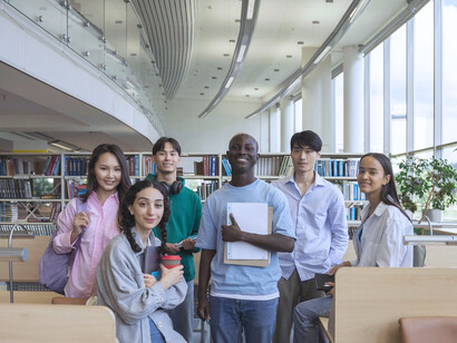 A group of students smiling in a library, representing how literacy and access to education is key for development 