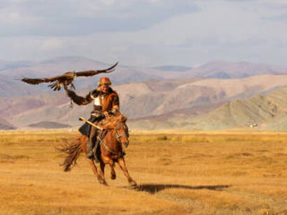 A Kazakh eagle hunter gallops across the river, his golden eagle perched on his arm, embodying the ancient bond between humans and nature in the vast steppes
