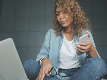 A woman in denim jeans working on a laptop while sitting on a bed