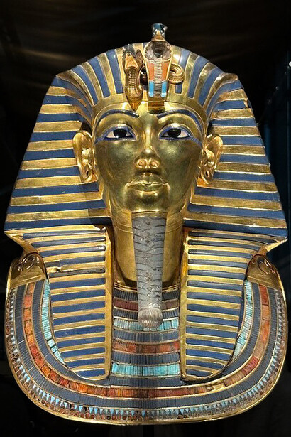 The golden funerary mask of Tutankhamun, featuring a striped nemes headdress and protective cobra and vulture symbols, at the Grand Egyptian Museum, Giza, Egypt