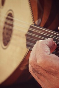 Weathered hands gliding across the oud’s strings, representing the preservation of Morocco’s musical memory