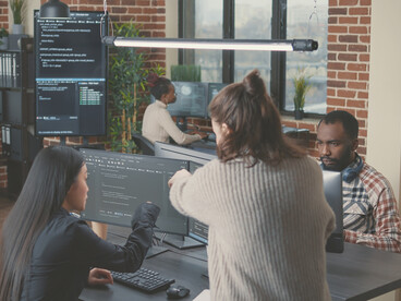 Team of database administrators analyzing source code on a wall screen while developers use AI to compare error
