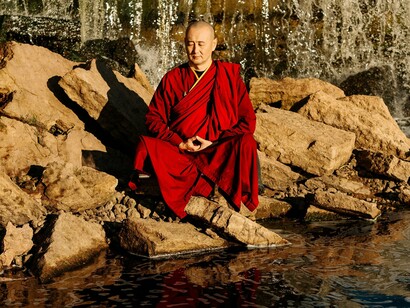A serene monk seated in meditation near flowing water, symbolizing the calming power of mindful awareness