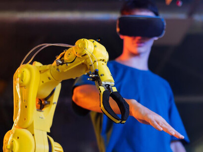 A person wearing protective glasses works hands-on with a robot in a state-of-the-art robotics laboratory