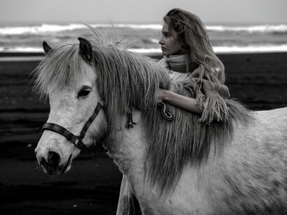 A woman holds onto her horse lovingly on a beach during a cloudy day