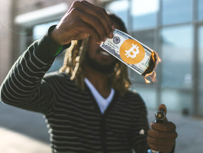 A man wearing a black striped long-sleeve shirt burns a ripped banknote, representing financial collapse