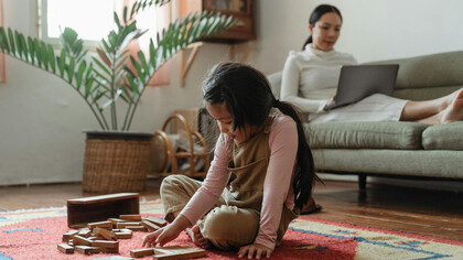 Niña con juguetes y mujer recostada en un sillón con una computadora