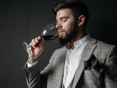 Oenologie. L'expert tient le grand verre-ballon par le pied, le tourne avec fermeté et ampleur, le regarde avec attention, hume le vin, plonge son nez de nouveau

